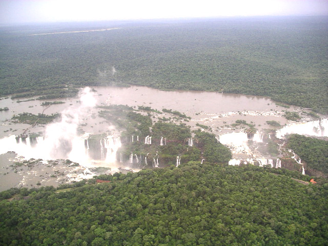 The aerial view of Iguazu Falls from a helicopter, showing the width of the falls and the mixture of massive wide cascades and individual drops, separated by outcrops and islands.