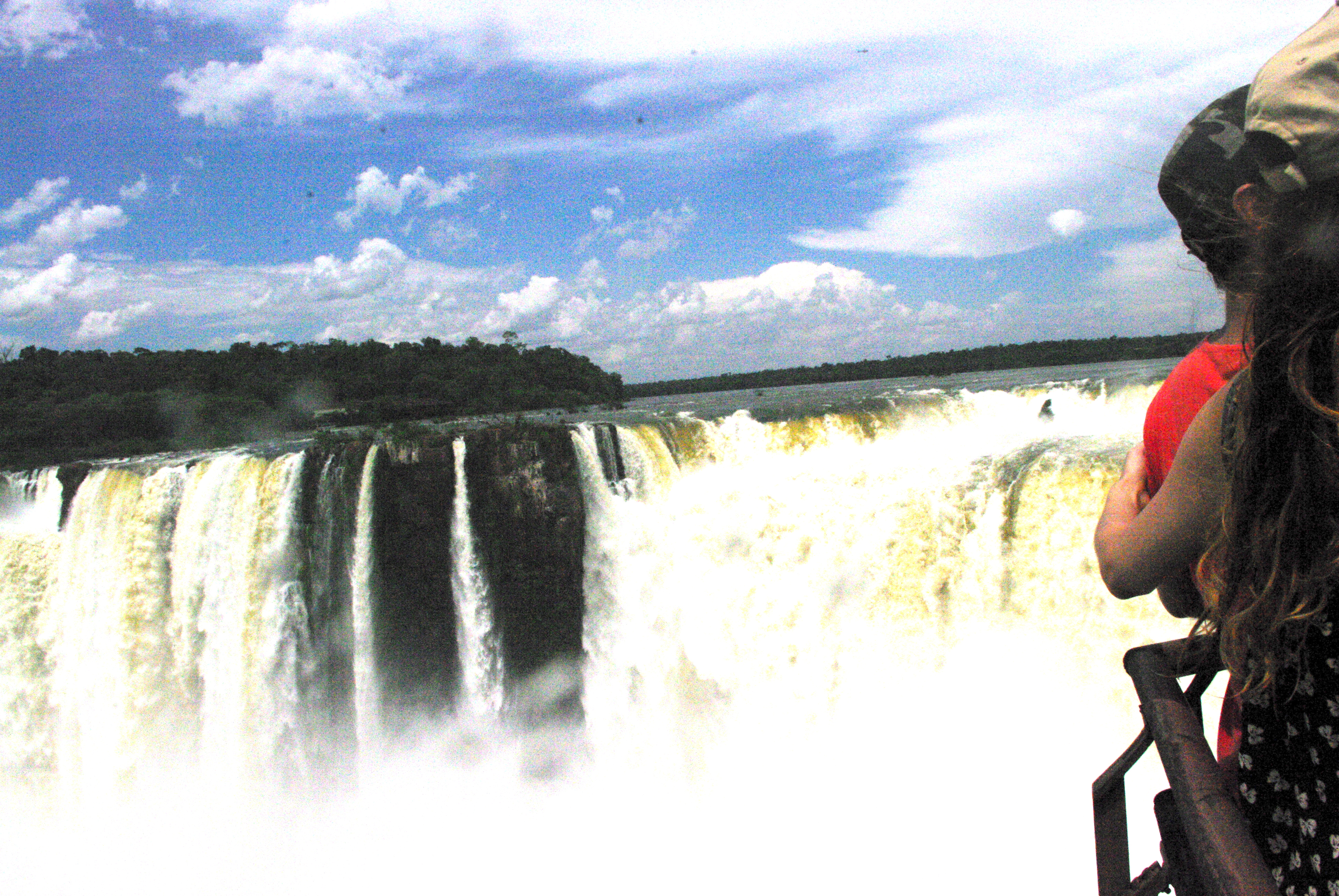 Standing with a friend and looking across Iguazu Falls from a viewing platform . You can see the mixtue of great cascading white sheets and much smaller single waterfalls.