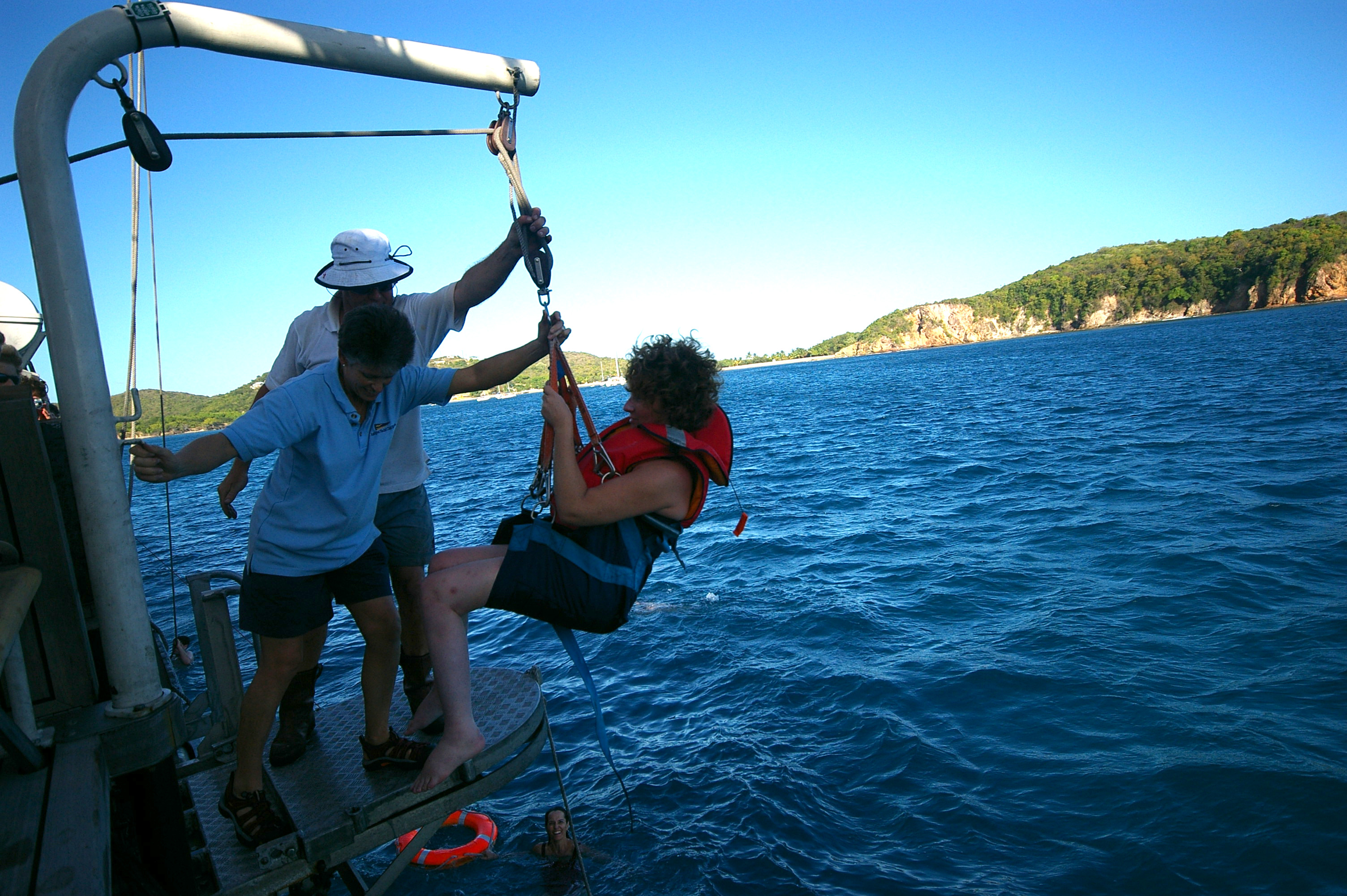 Two of the crew guiding  someone from the main deck on the hoist as they start to lower them into the water. 